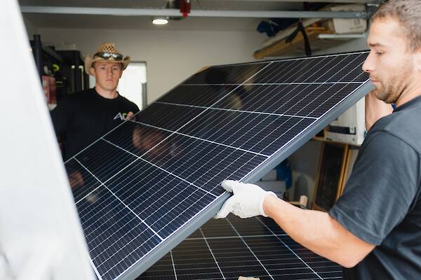 Zwei Arbeiter transportieren eine Solarplatte.